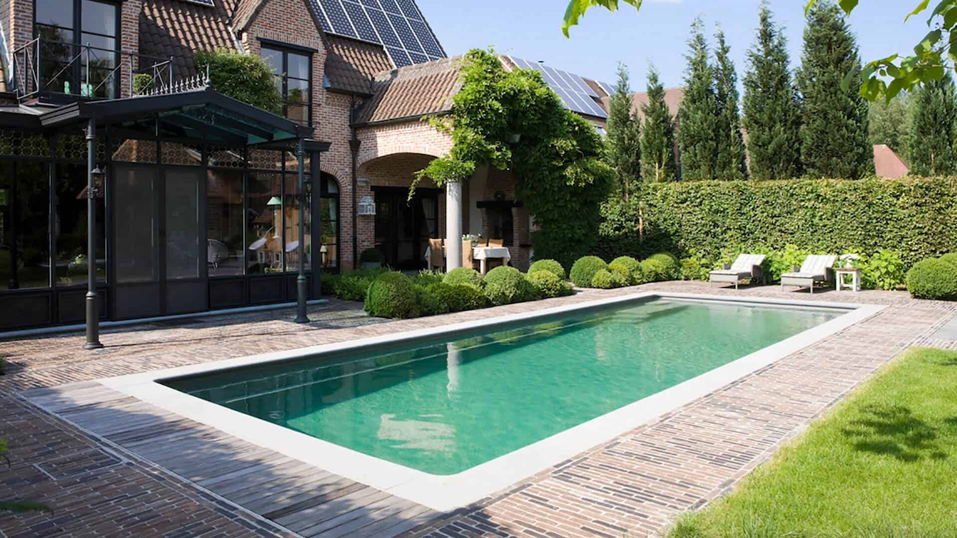 Traditional-style brick house with solar panels and a rectangular garden pool bordered by lush greenery and brick paving.