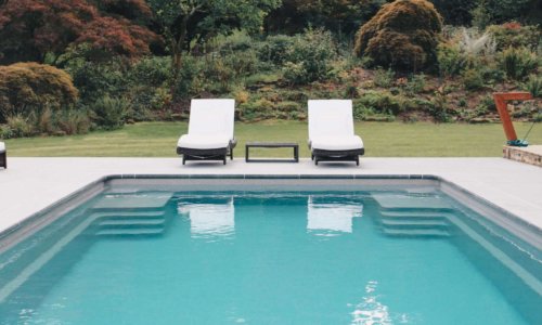Elegant garden pool with two white sun loungers overlooking manicured lawns and leafy trees.