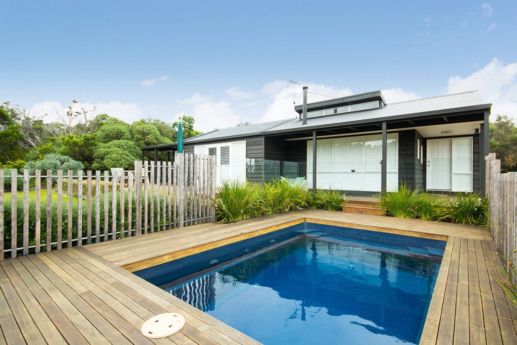 Contemporary home with a small square plunge pool and timber decking, enclosed by a wooden fence and lush greenery.