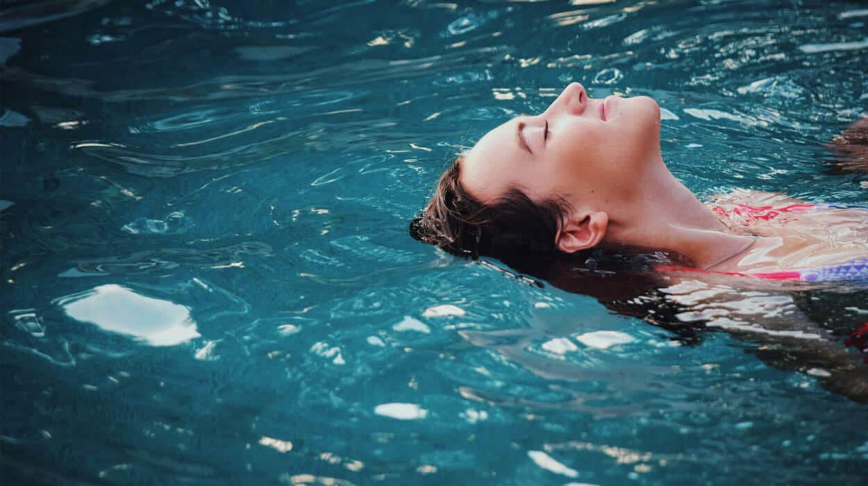 Woman floating peacefully on her back in clear blue pool water.