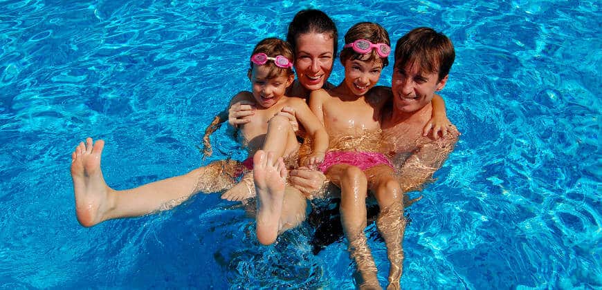 Happy parents with kids in swimming pool on summer vacation
