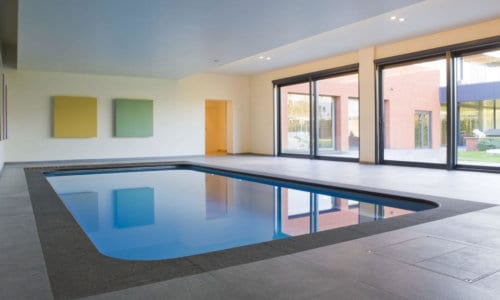Modern indoor swimming pool with clean architectural lines, large windows, and minimalist wall art.