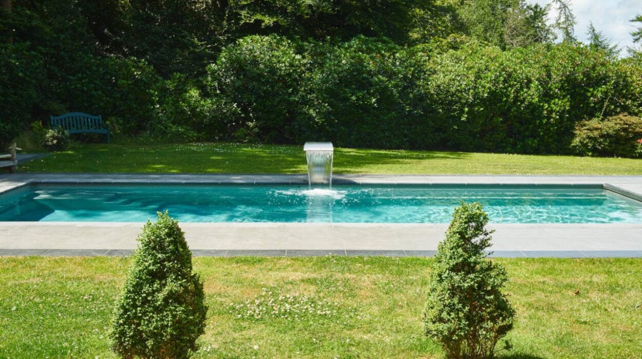 Luxury rectangular garden pool in New Forest, Hampshire, with a central waterfall feature and lush greenery in the background.