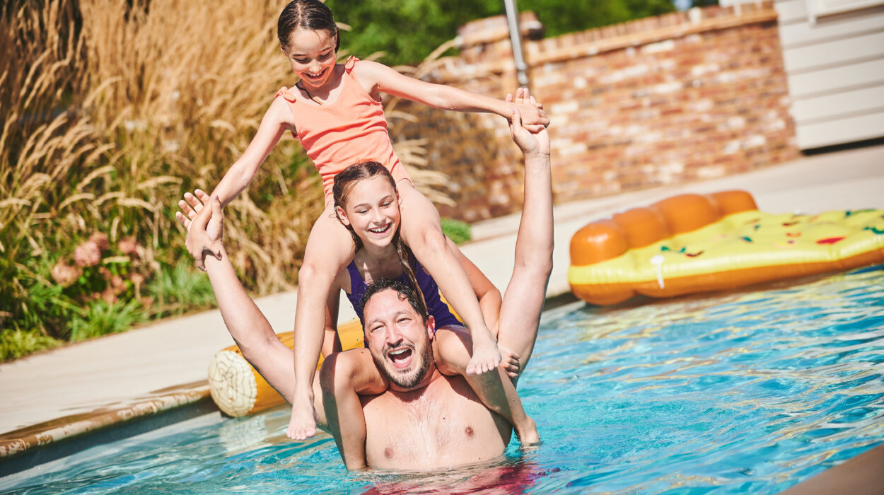 Kids in pool playing with dad on summers day.