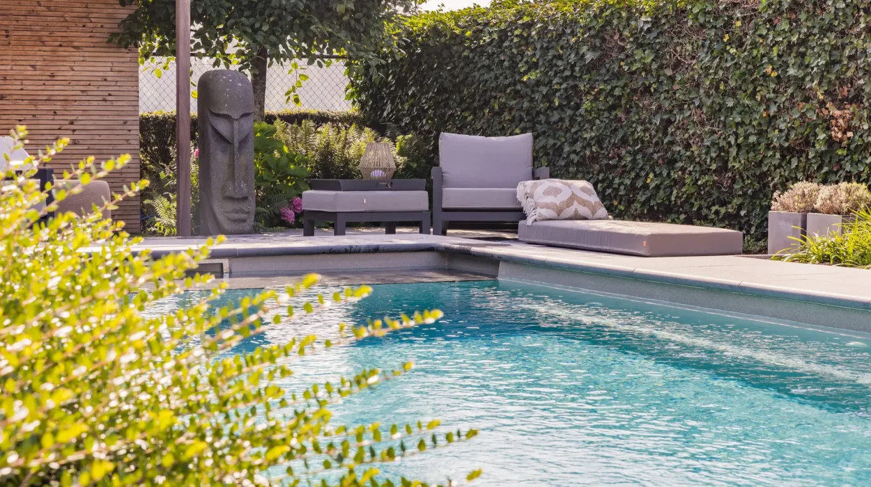 Bohemian outdoor living space with a swimming pool, cushioned sun loungers, tropical plants, and a decorative stone sculpture.